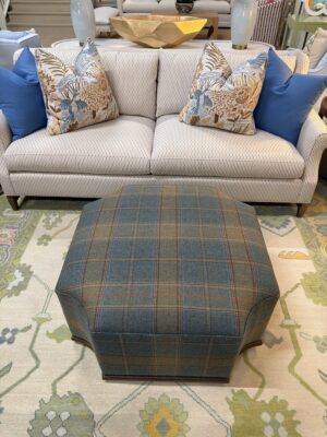 Furrow ottoman covered in wool plaid with a wooden base and gold nail heads